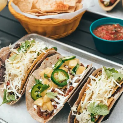 Tacos on a tray in front of a basket of tortilla chips and a teal bowl of salsa